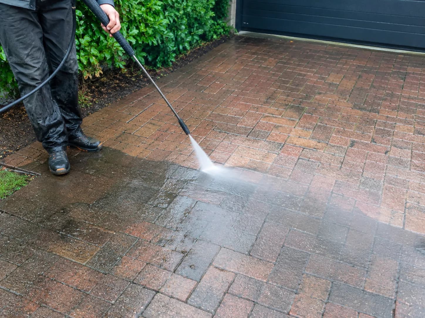 A block-paved driveway being pressure washed, the cleaned strip back to red brick